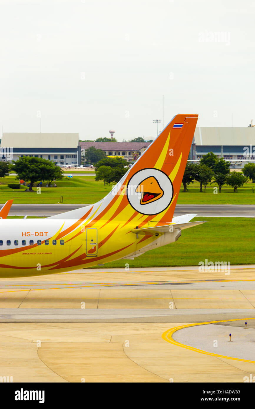 A golf course and golfers visible behind the tail section and logo of low cost carrier, Nok Air airplane taxiing on runway Stock Photo