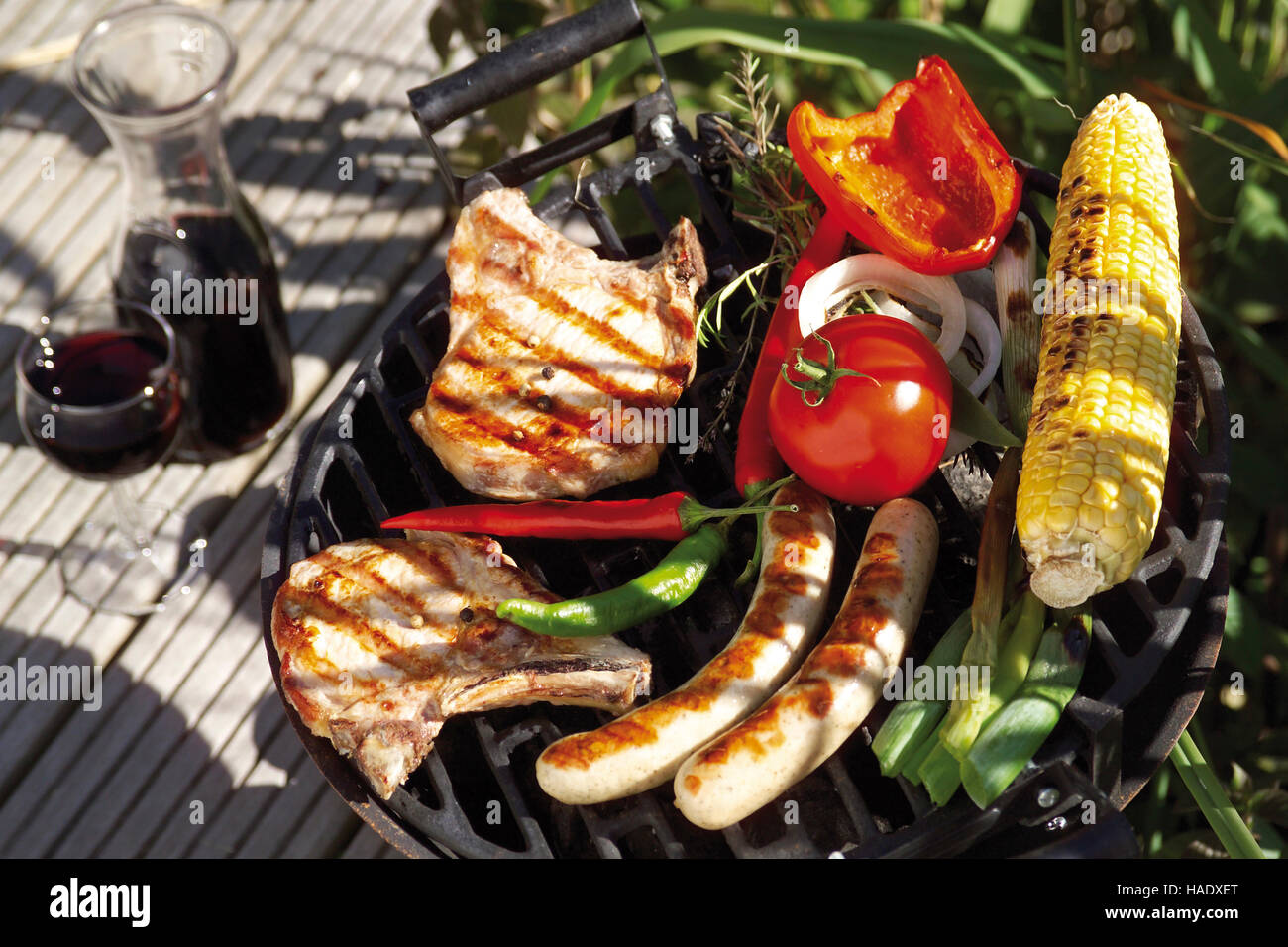Outdoor barbecue, meat chops, sausages, tomatoes, red wine, corn on the cob, peppers Stock Photo
