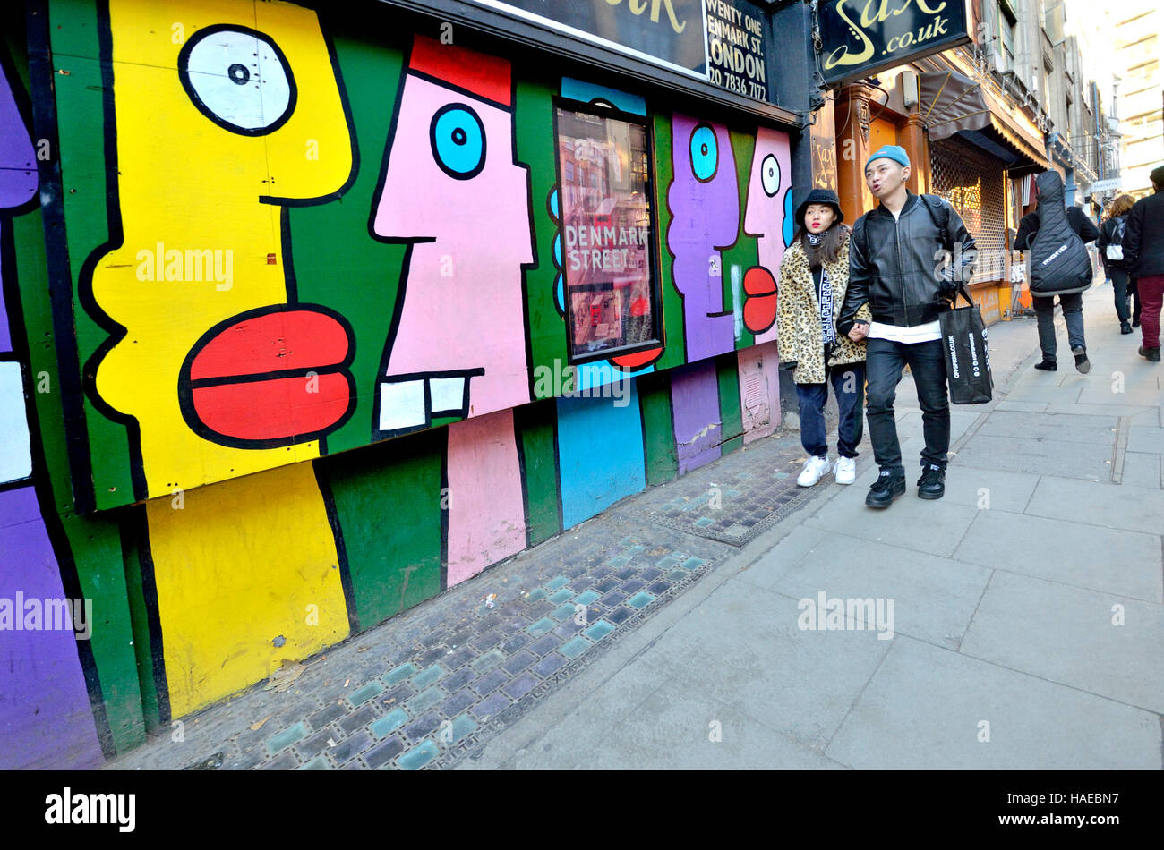 London, England, UK. Denmark Street people walking past Thierry Noir