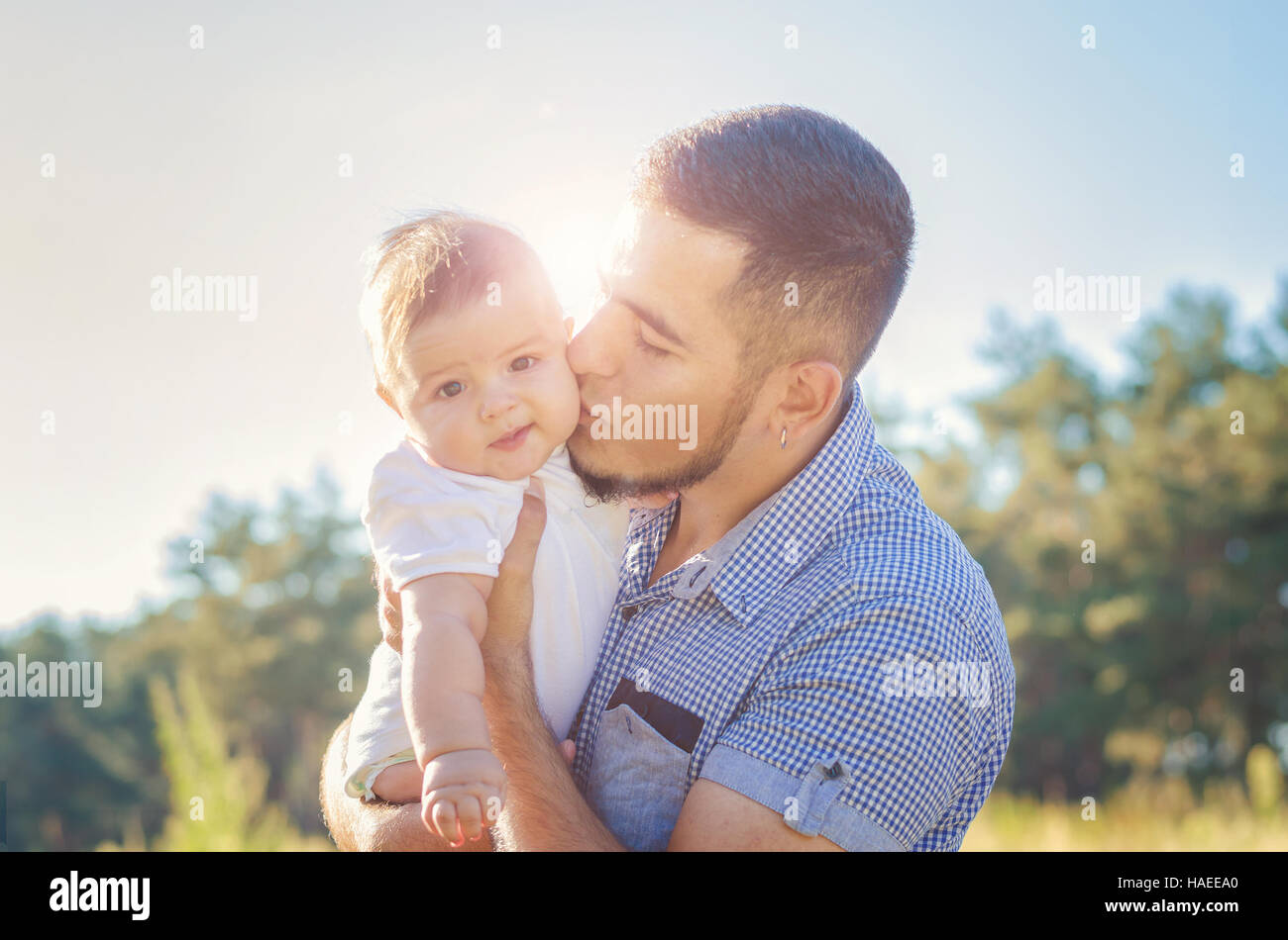 Young daddy kissing a baby. Walk autumn evening outdoors. Solar flare illuminates the baby and dad. Stock Photo
