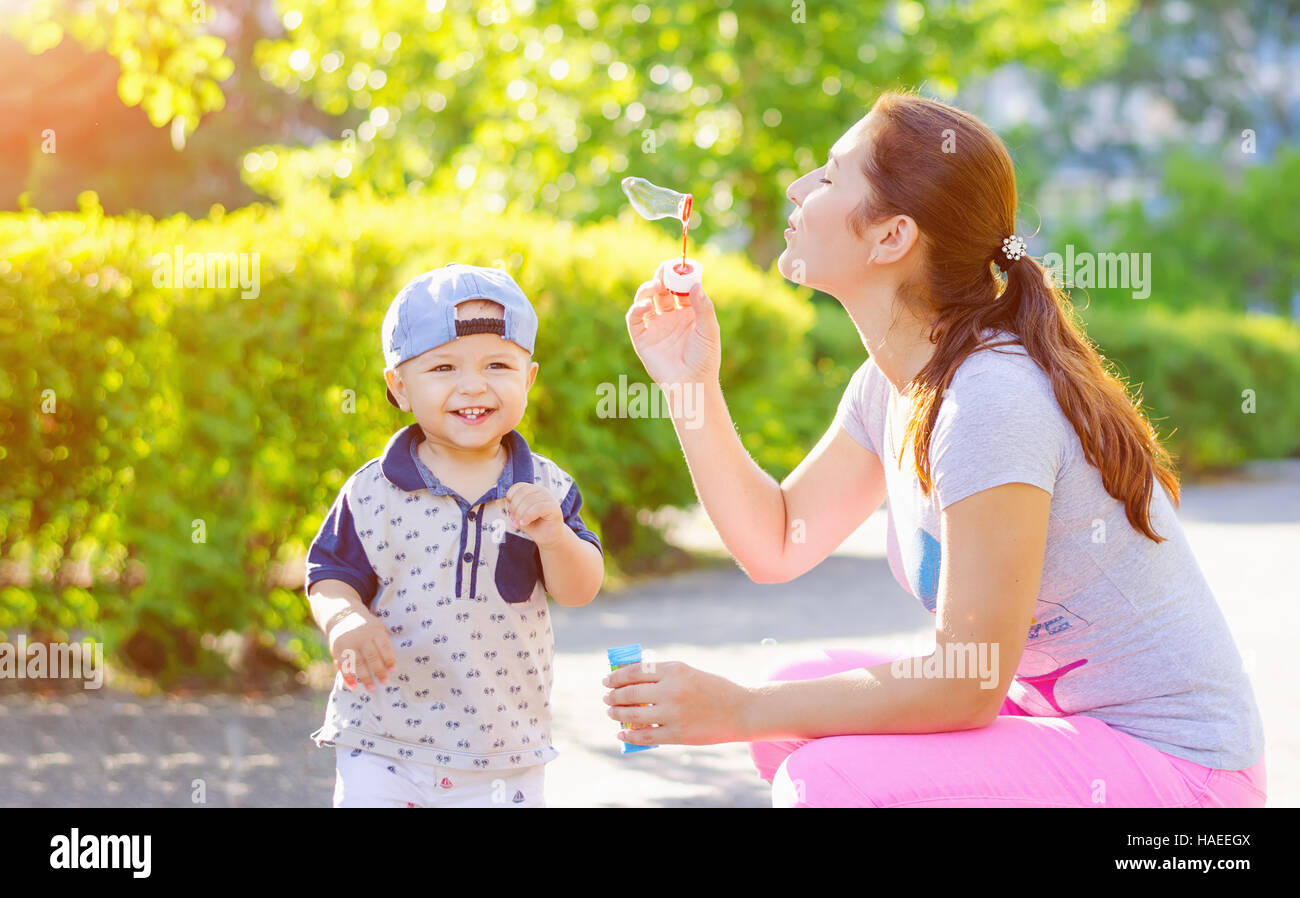 Mother with a little son laughing outdoors blow bubbles. Walk in nature with sunlight. Stock Photo