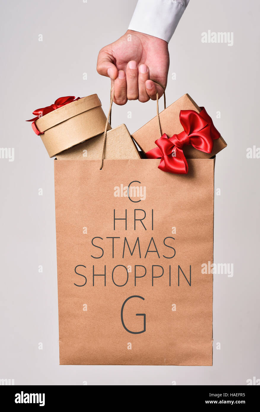 closeup of the hand of a young caucasian man holding a paper shopping bag full of gifts and the text christmas shopping written in it forming a christ Stock Photo