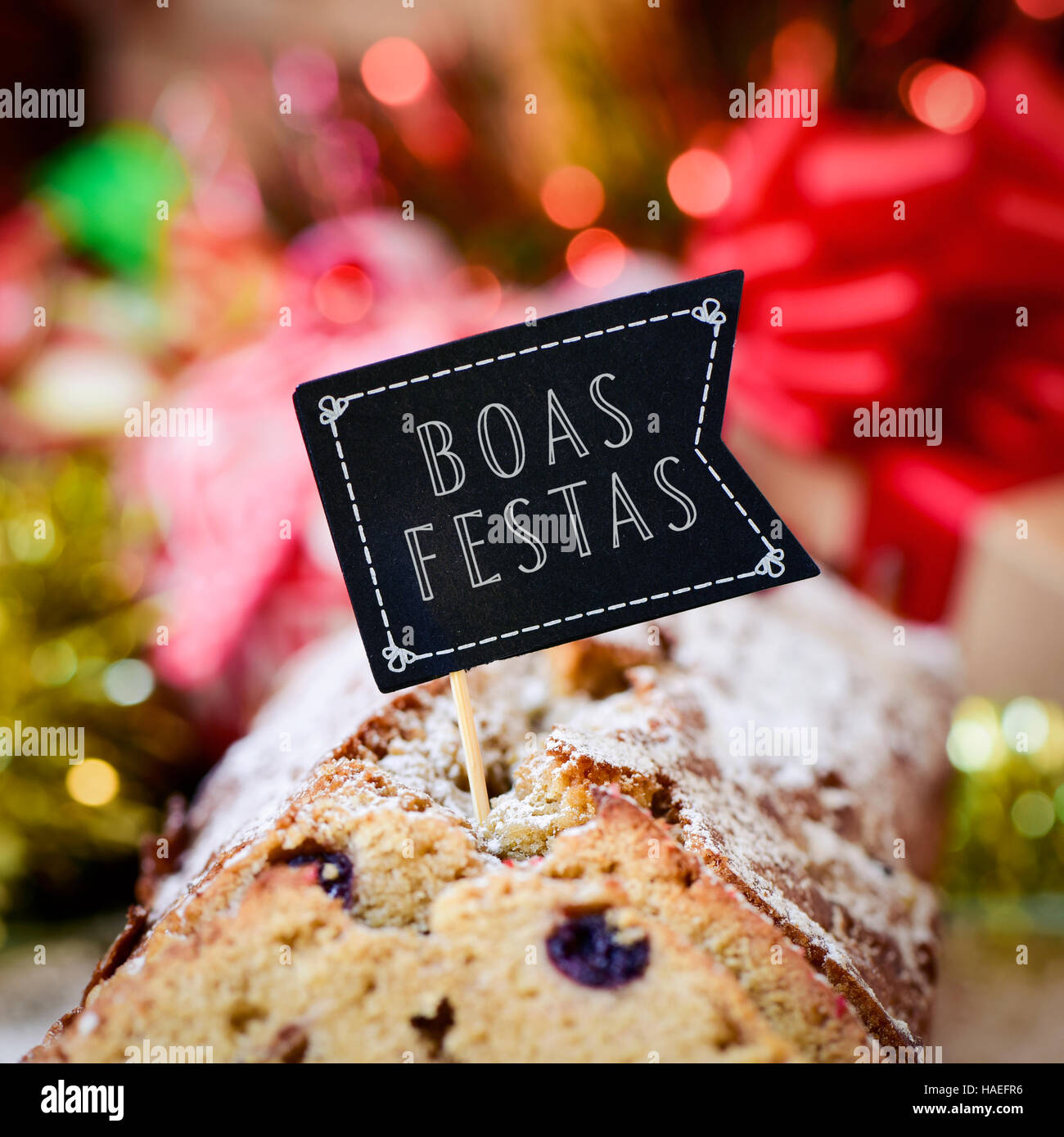 closeup of a fruitcake topped with a flag-shaped signboard with the text boas festas, happy holidays written in portuguese, on a table full of christm Stock Photo