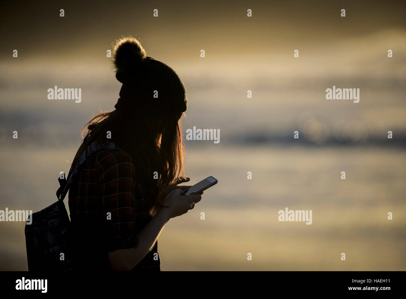 A girl wearing a woollen hat texting on her mobile phone. Stock Photo