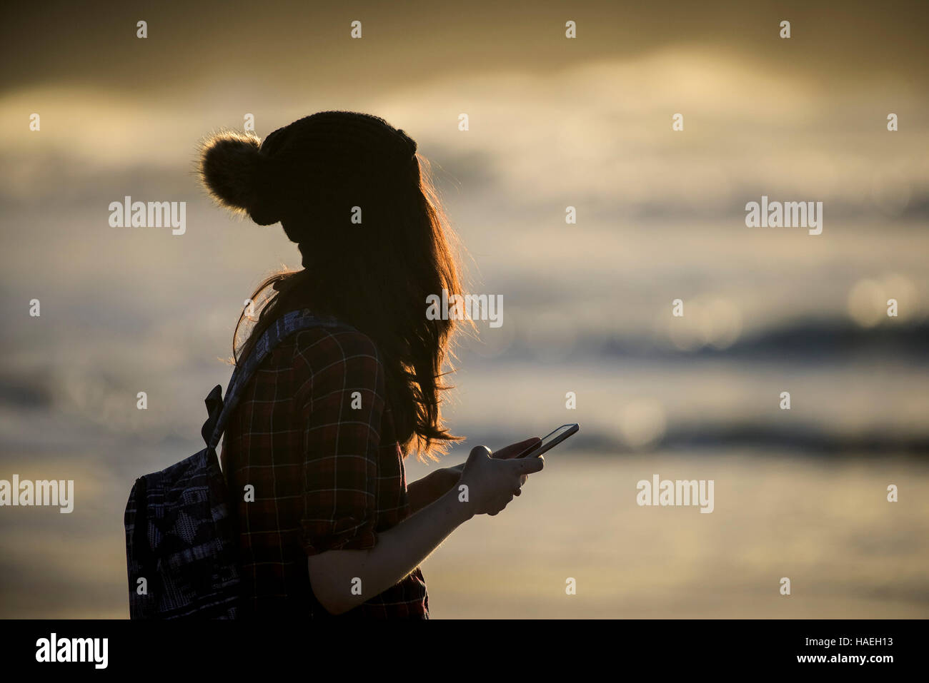 A girl wearing a woollen hat texting on her mobile phone. Stock Photo