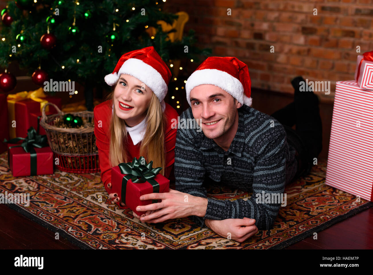 Man and woman lying near the Christmas tree in the hat of Santa Claus ...