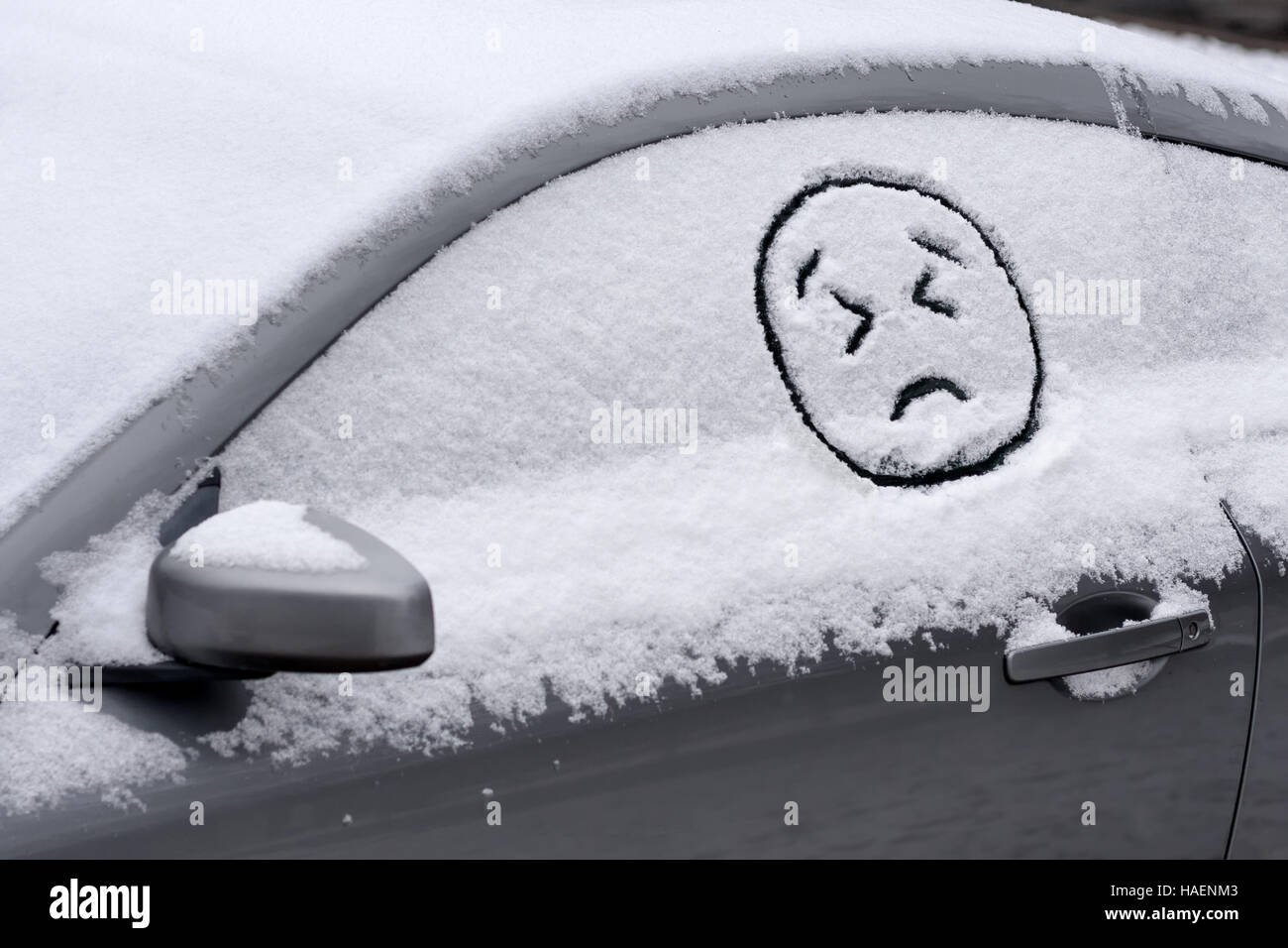 Sad Angry Emoji Face on snow covered car window - frustration, disgust, disappointment about winter early snowfall Stock Photo