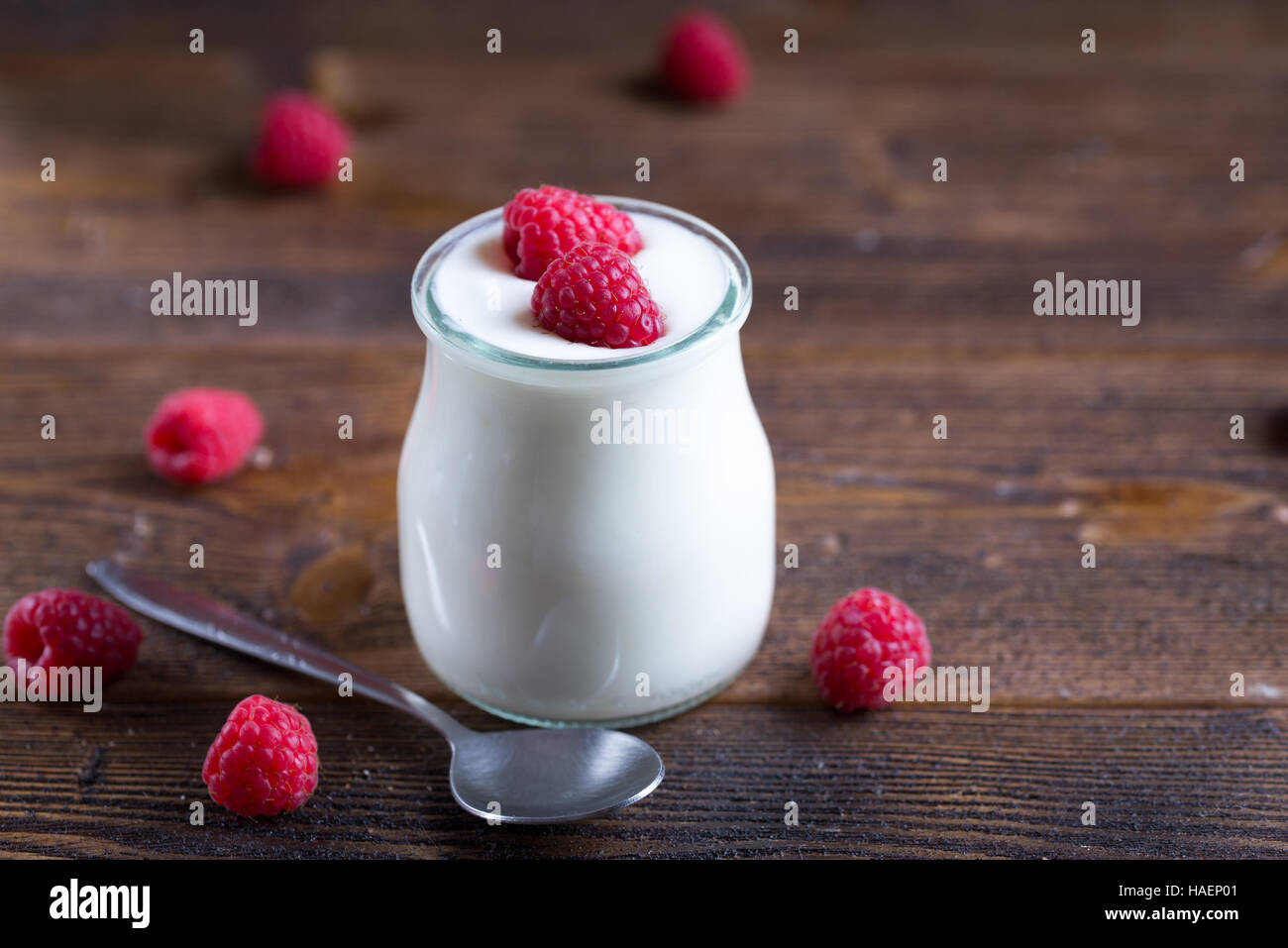 White yogurt with raspberries in glass bowl on rustic table. Stock Photo