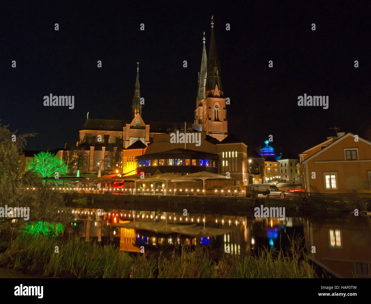 A scenic view of the west side of Fyris river by night with Uppsala Cathedral behind a market hall with restaurants Sweden Stock Photo