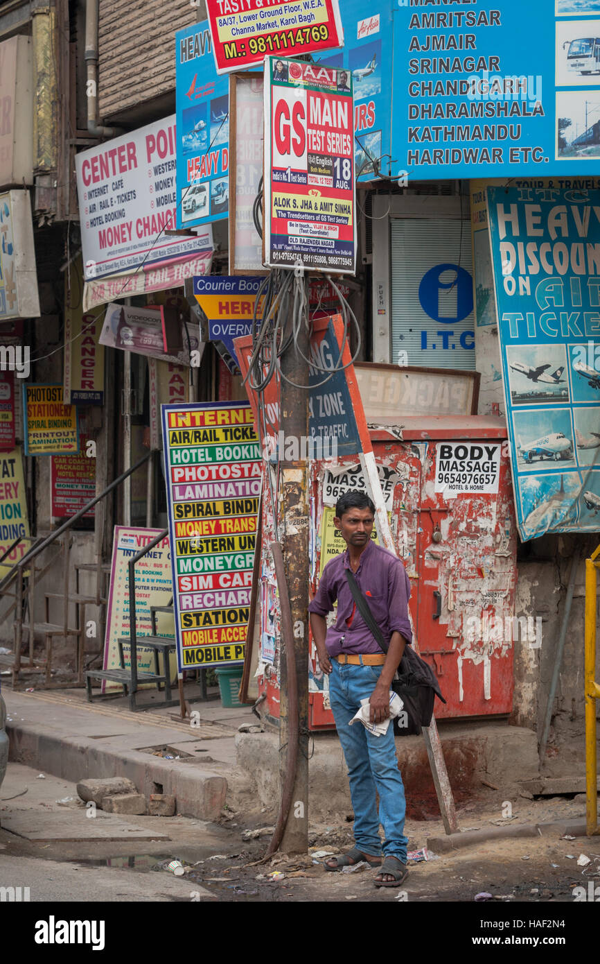 A man standing on a street corner in Old Delhi, India, shwoing a mass of advertisinf hoardings for shops and services. Stock Photo