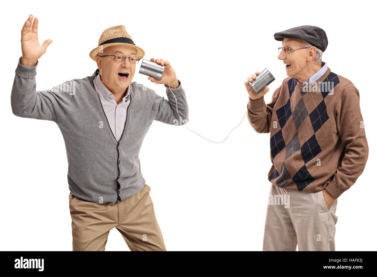 Cheerful seniors telling jokes to each other through a tin can phone isolated on white background Stock Photo