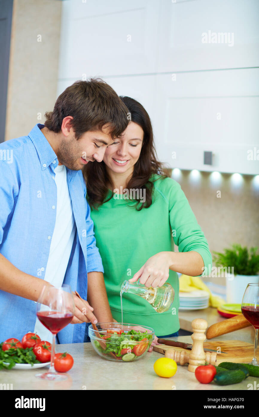 Adding Fresh Oil Young woman adding olive oil into fresh salad while her husband mixing ...