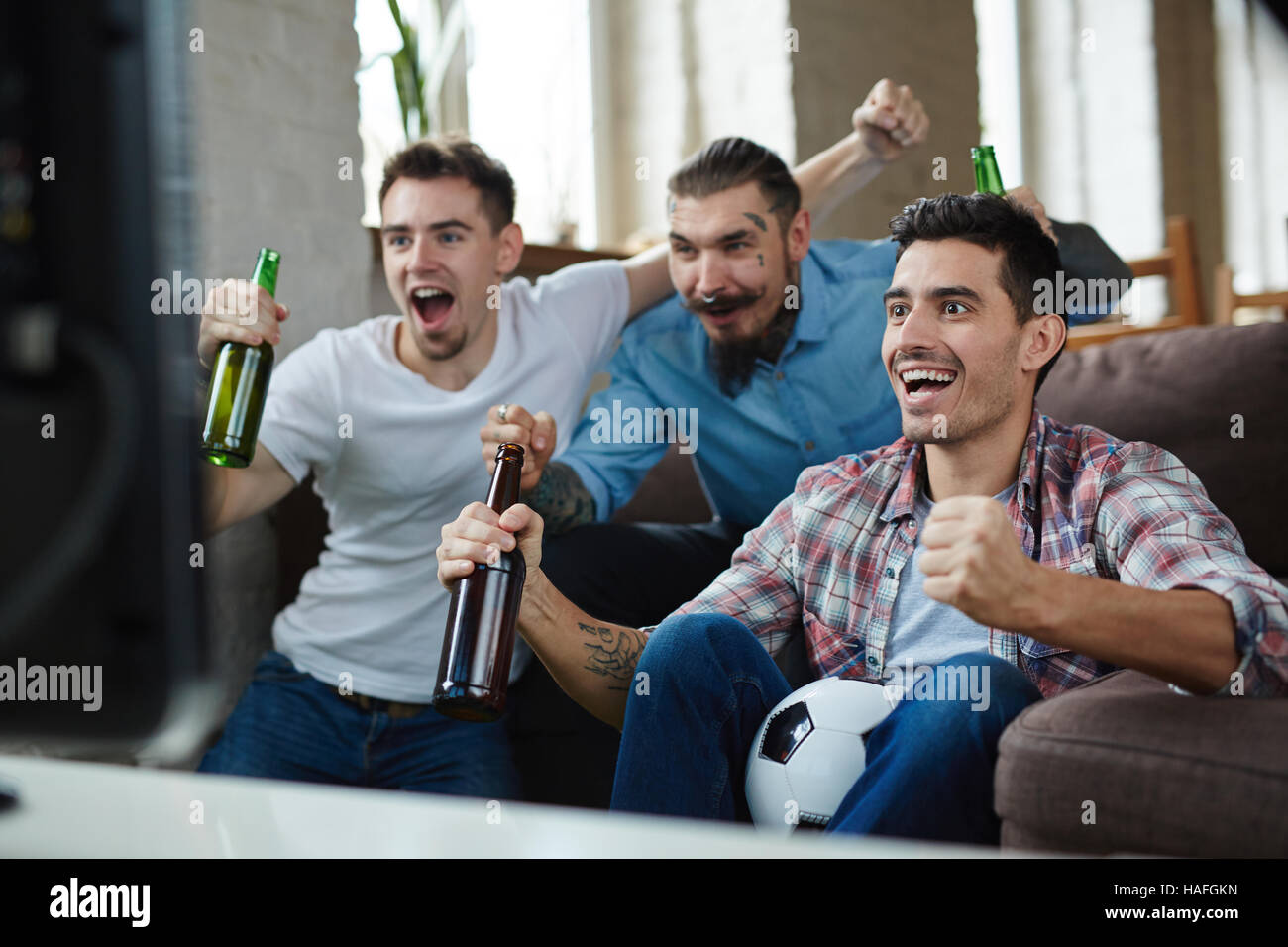 Ecstatic guys showing their gladness with triumph gesture in front of tv set Stock Photo