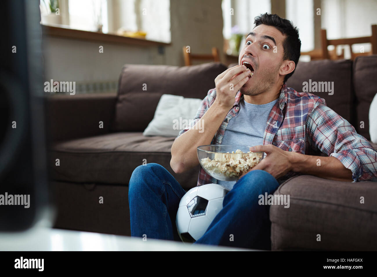 Astonished guy eating popcorn while watching curious tv program Stock Photo