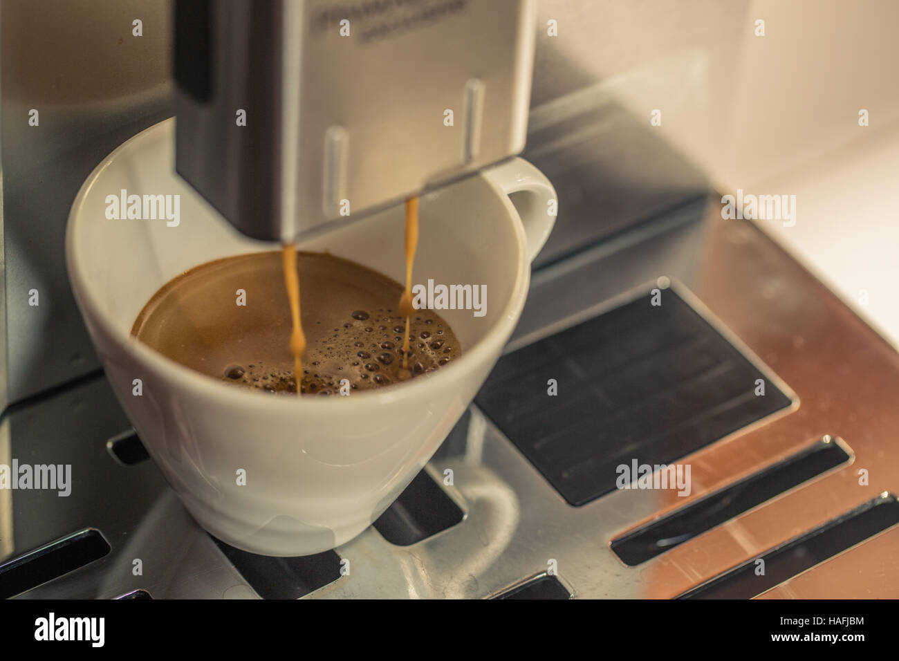 Closeup of coffee pouring from coffee machine into white cup at