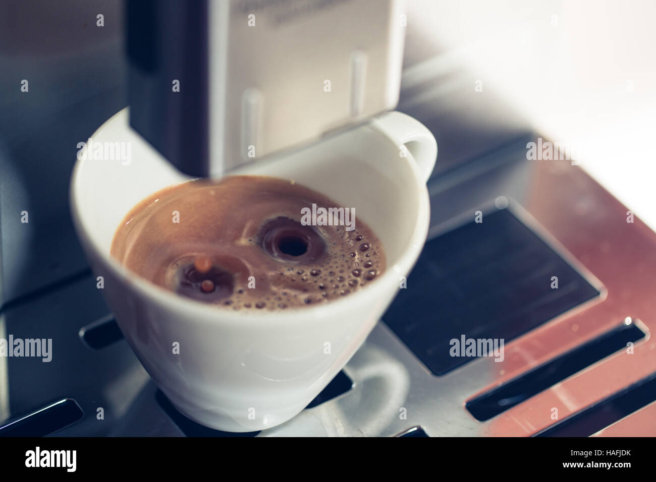Closeup of coffee pouring from coffee machine into white cup at