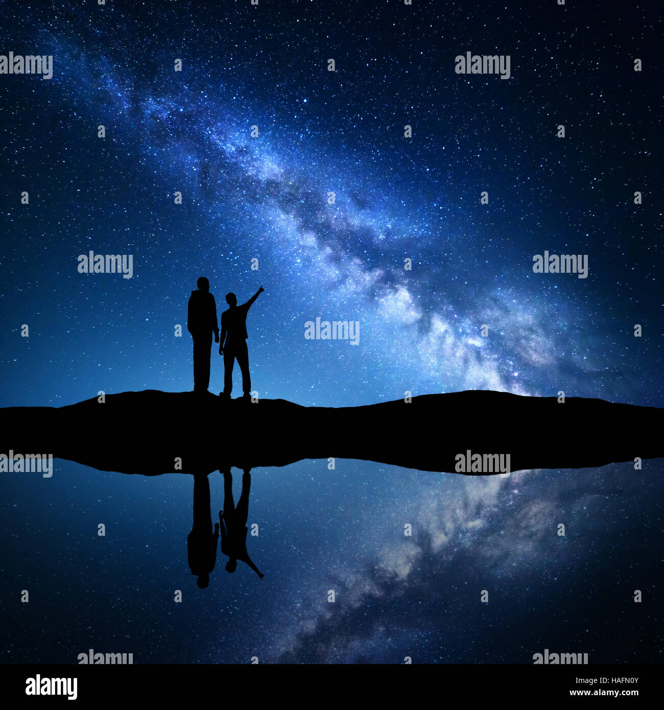 Milky Way with silhouette of a family. Father and a son who pointing finger in night starry sky on the mountain near the river Stock Photo