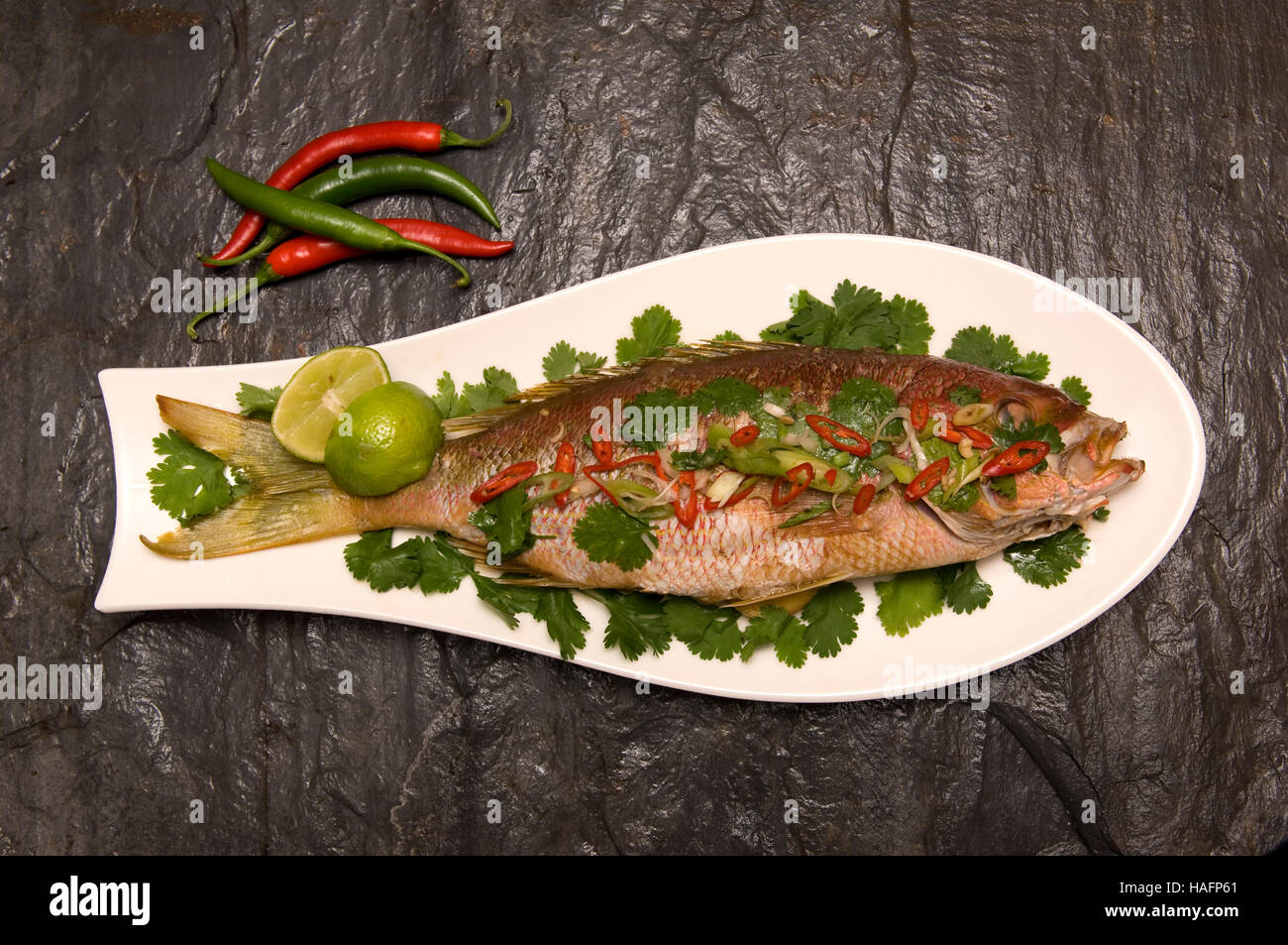 A whole cooked seabass on a fish-shaped white dish sitting on a dark