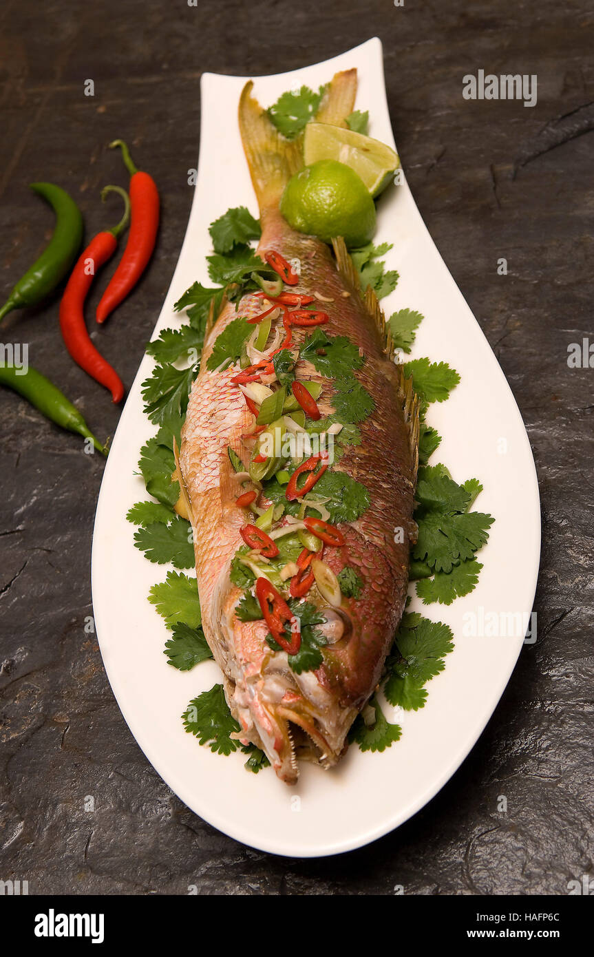 A whole cooked seabass on a fish-shaped white dish sitting on a dark
