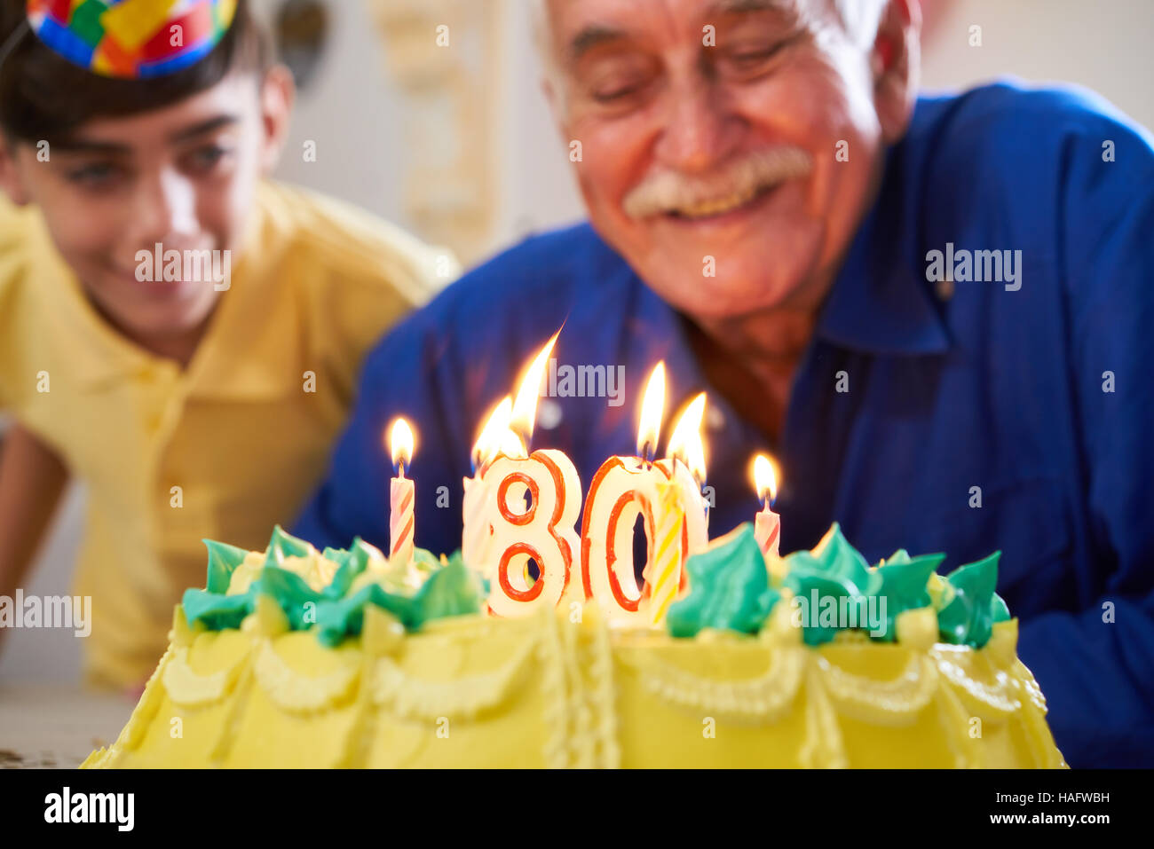 Grandson and family celebrating senior man eighty birthday. Grandfather blowing candles with number 80 on cake and smiling. Stock Photo