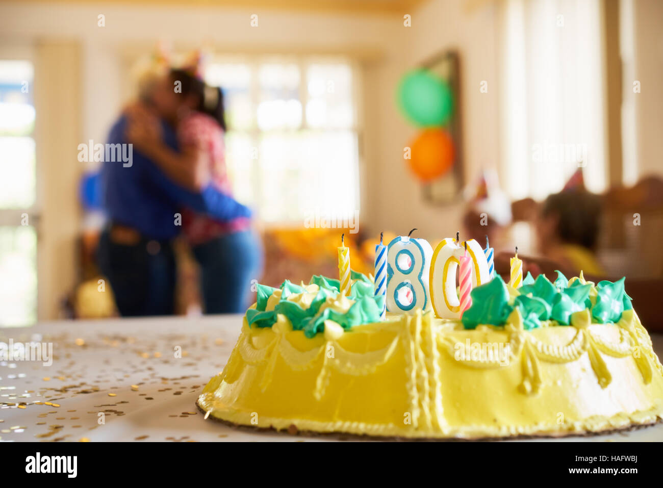 Woman embracing her senior dad at birthday party, celebrating his eighty years in retirement home. Focus on cake on table. Stock Photo