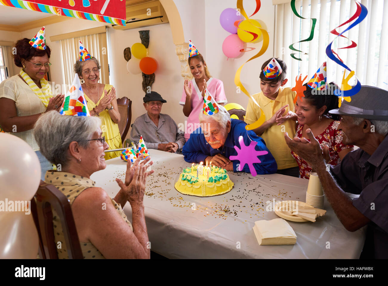 Group of old friends and family celebrating senior man 80 birthday party in retirement home. Happy elderly people having fun. Grandfather blowing cand Stock Photo