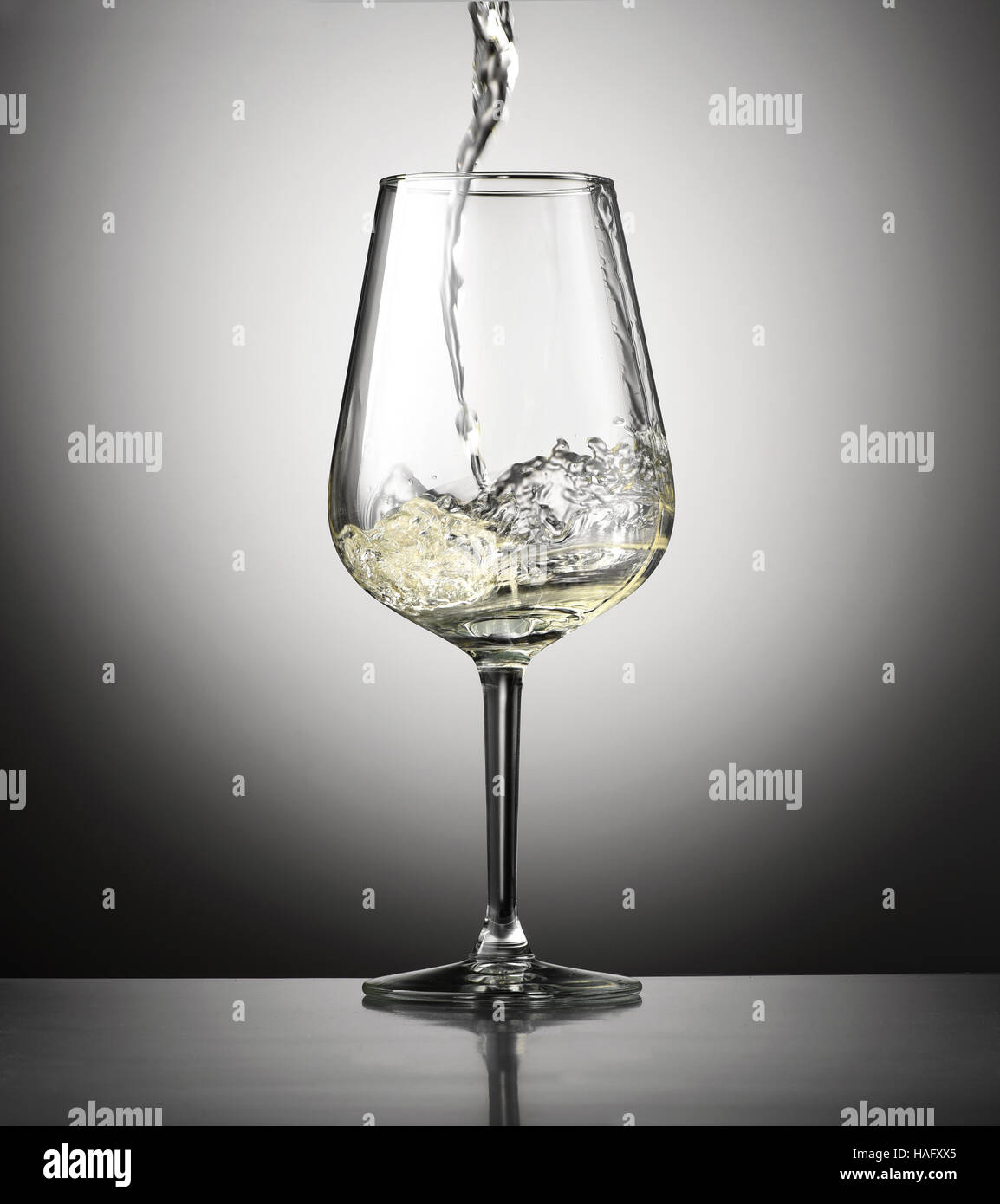 Pouring white wine into a stylish wineglass from above, side view over a gray background with vignette in a viticulture concept Stock Photo
