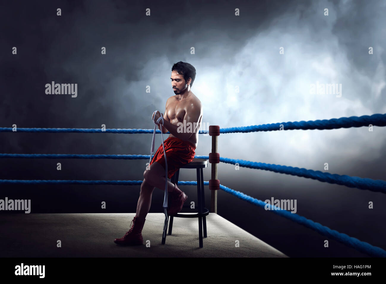 Sporty asian boxer man sitting on ring while wearing strap on wrist Stock Photo