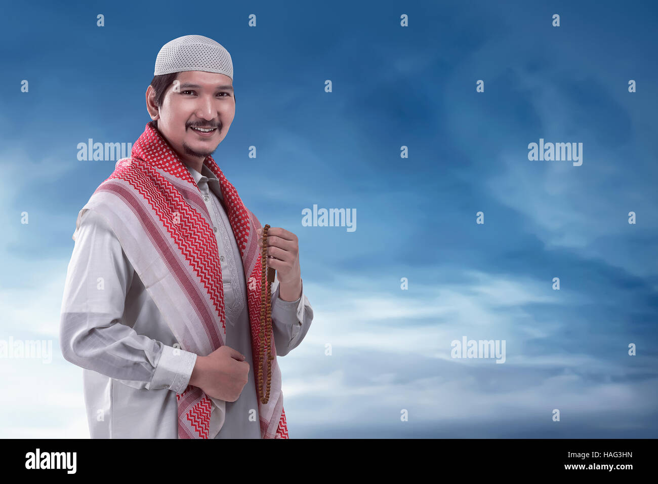 Young muslim asian man with cap and rosary on his hand, blue sky ...