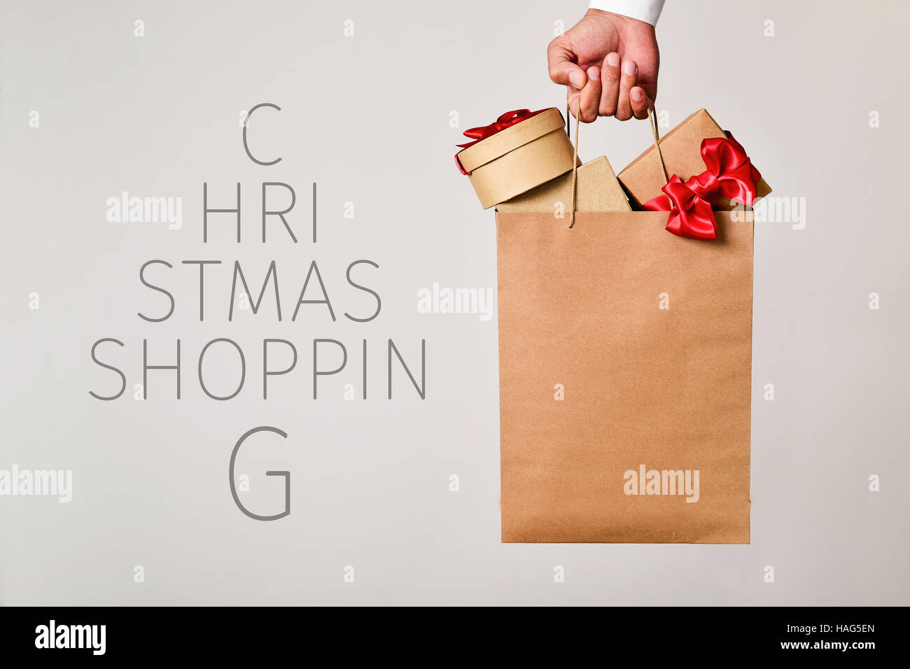 closeup of the hand of a young caucasian man holding a paper shopping bag full of gifts and the text christmas shopping forming a christmas tree Stock Photo
