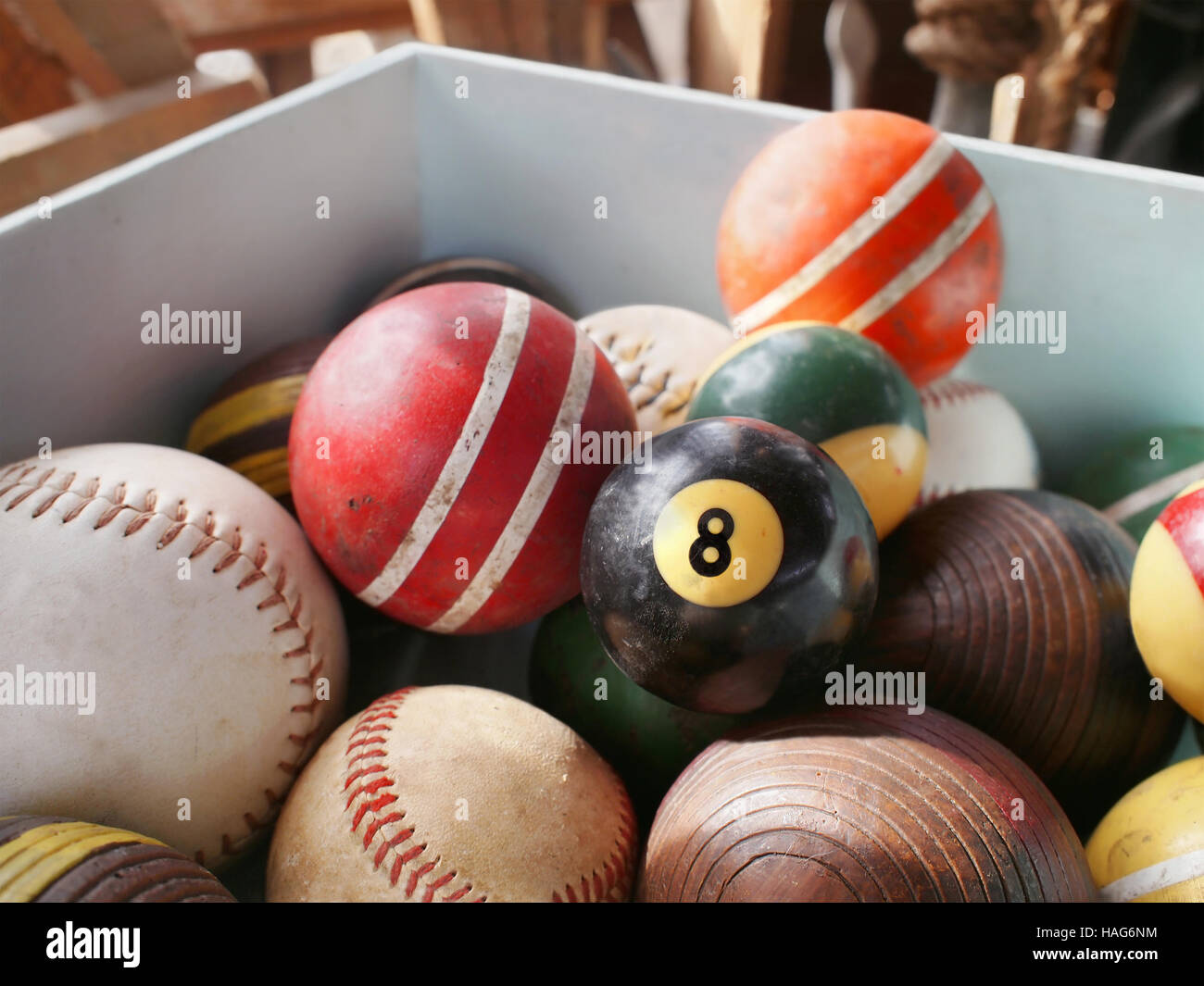 An old eight ball in wooden bin full of vintage game balls, including pool, croquet, and baseball. Stock Photo