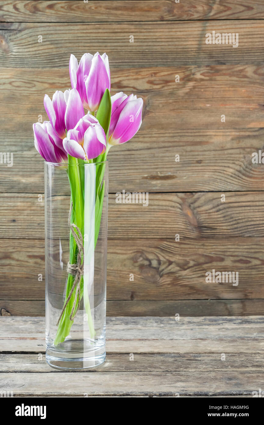 Beautiful tulip flowers in a glass vase on wooden table, floral backdrop Stock Photo