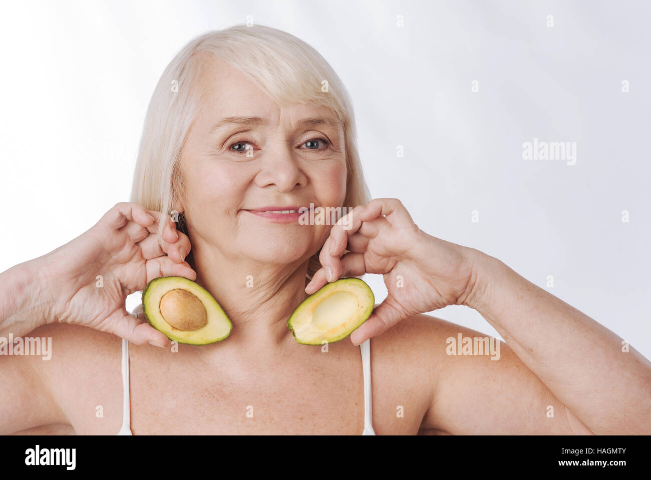 Optimistic aged woman having avocado halves in her hands Stock Photo