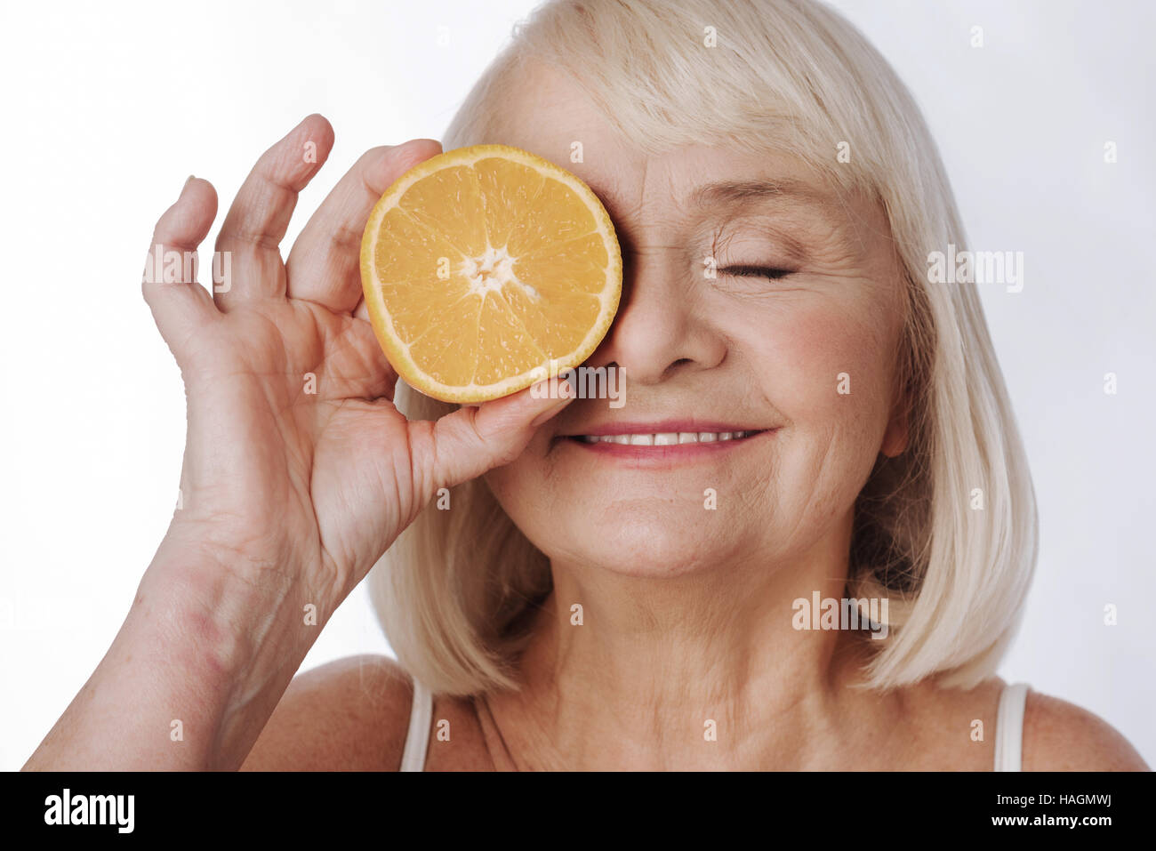 Nice elated woman putting an orange half to her eye Stock Photo