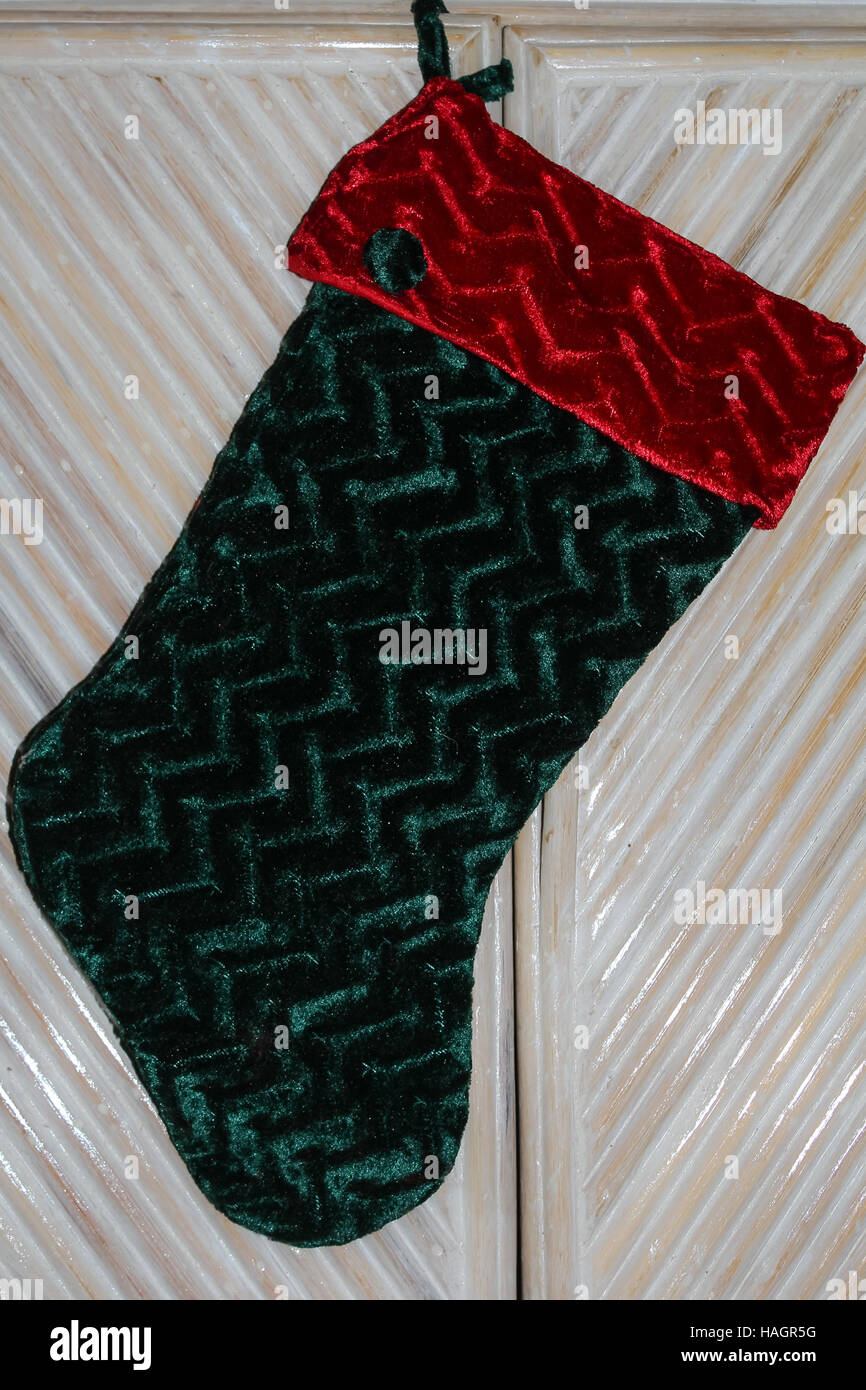 Christmas stocking of red and green textured velvet hanging from bamboo furniture for a home with no fireplace Stock Photo
