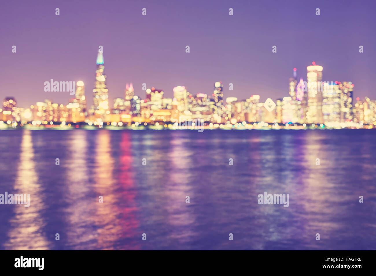 Vintage toned blurred Chicago city lights with reflection in Lake Michigan at night, urban abstract background. Stock Photo