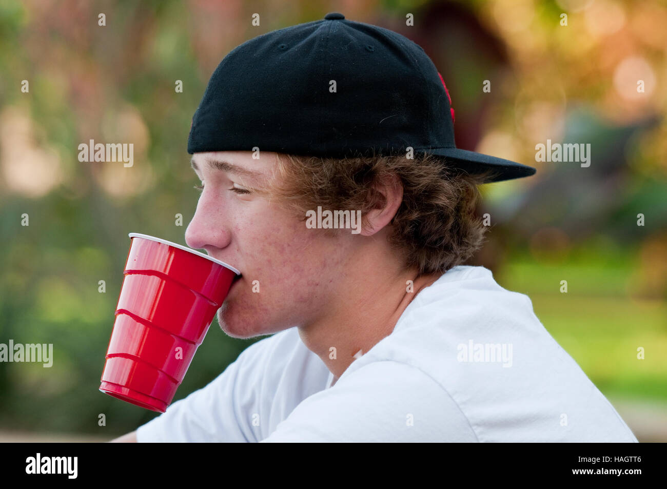 Teen boy outdoors with acne looking at camera with black backwards hat and white shirt. Stock Photo
