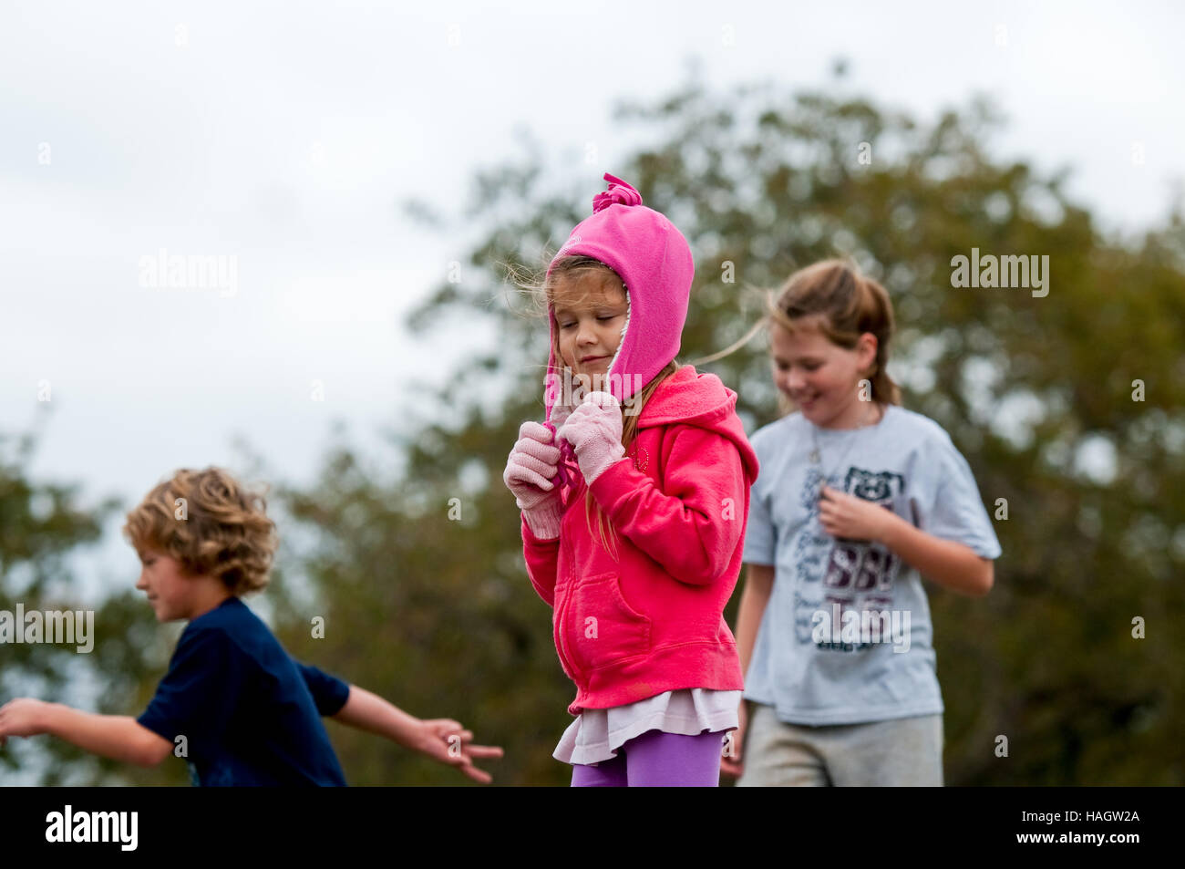 Happy Little girl bundled in pink winter clothes on a windy day with friends in background. Stock Photo
