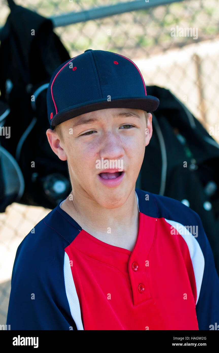 Teen baseball boy sitting in dugout with mouth open talking. Stock Photo