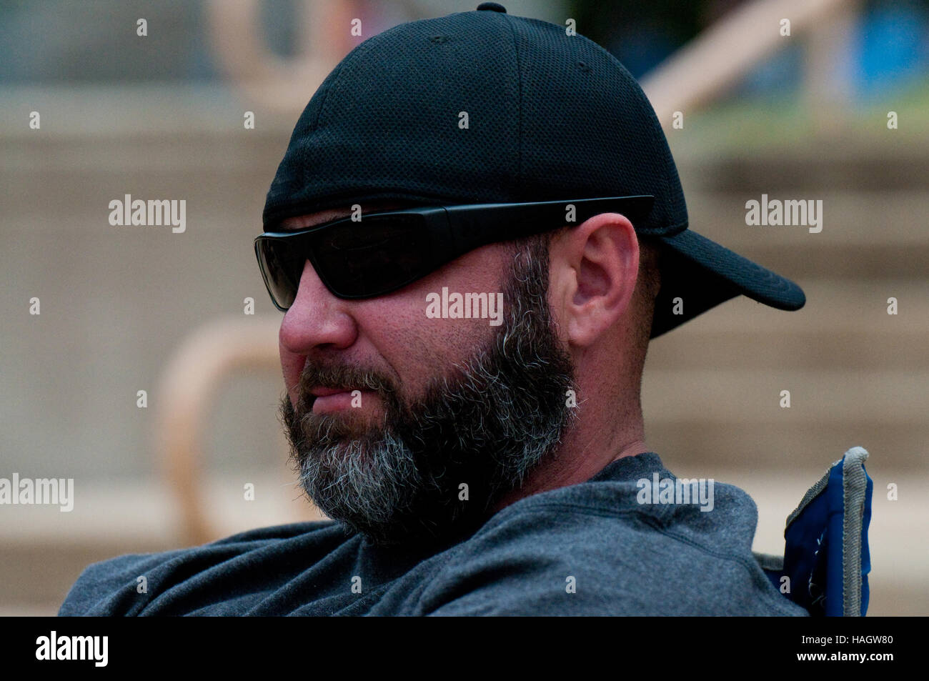 Middle-aged man with black and grey beard wearing sunglasses and hat backwards. Stock Photo