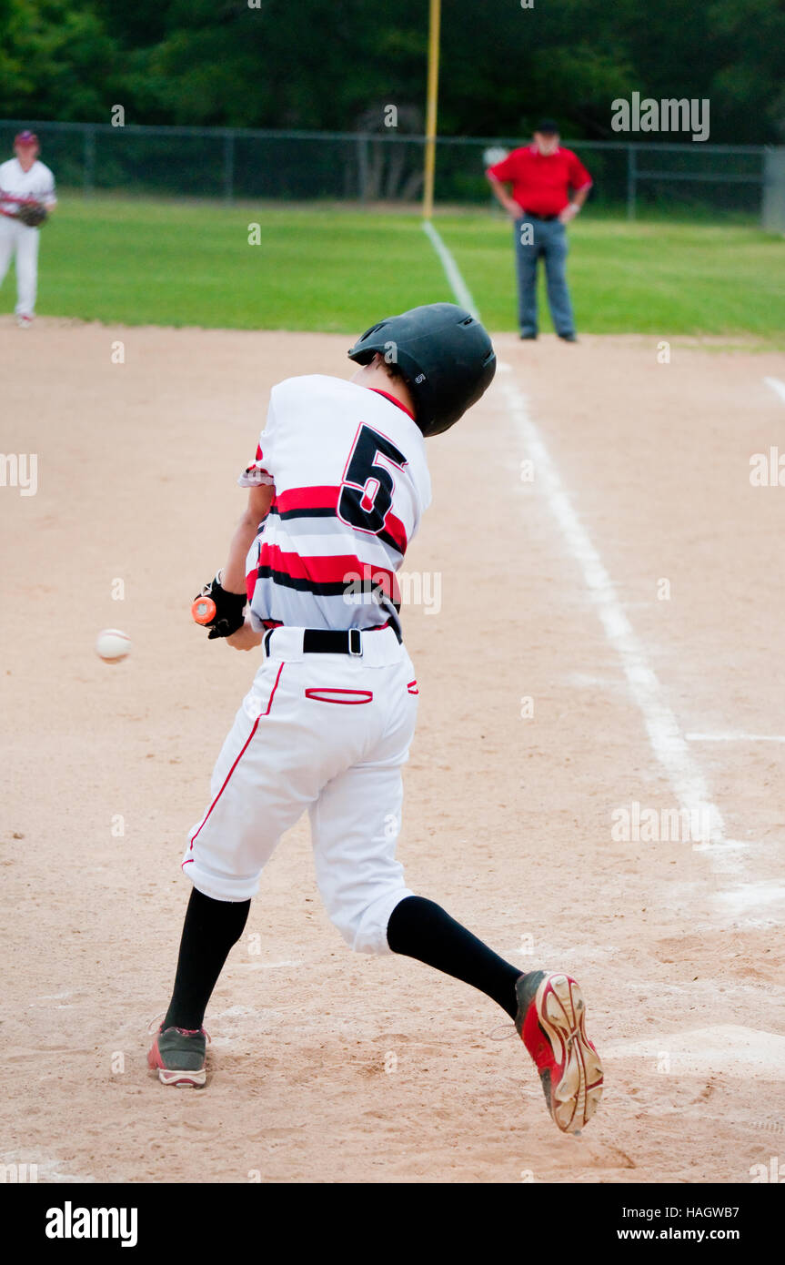 Teenage american baseball player swinging bat to hit the ball from behind. Stock Photo
