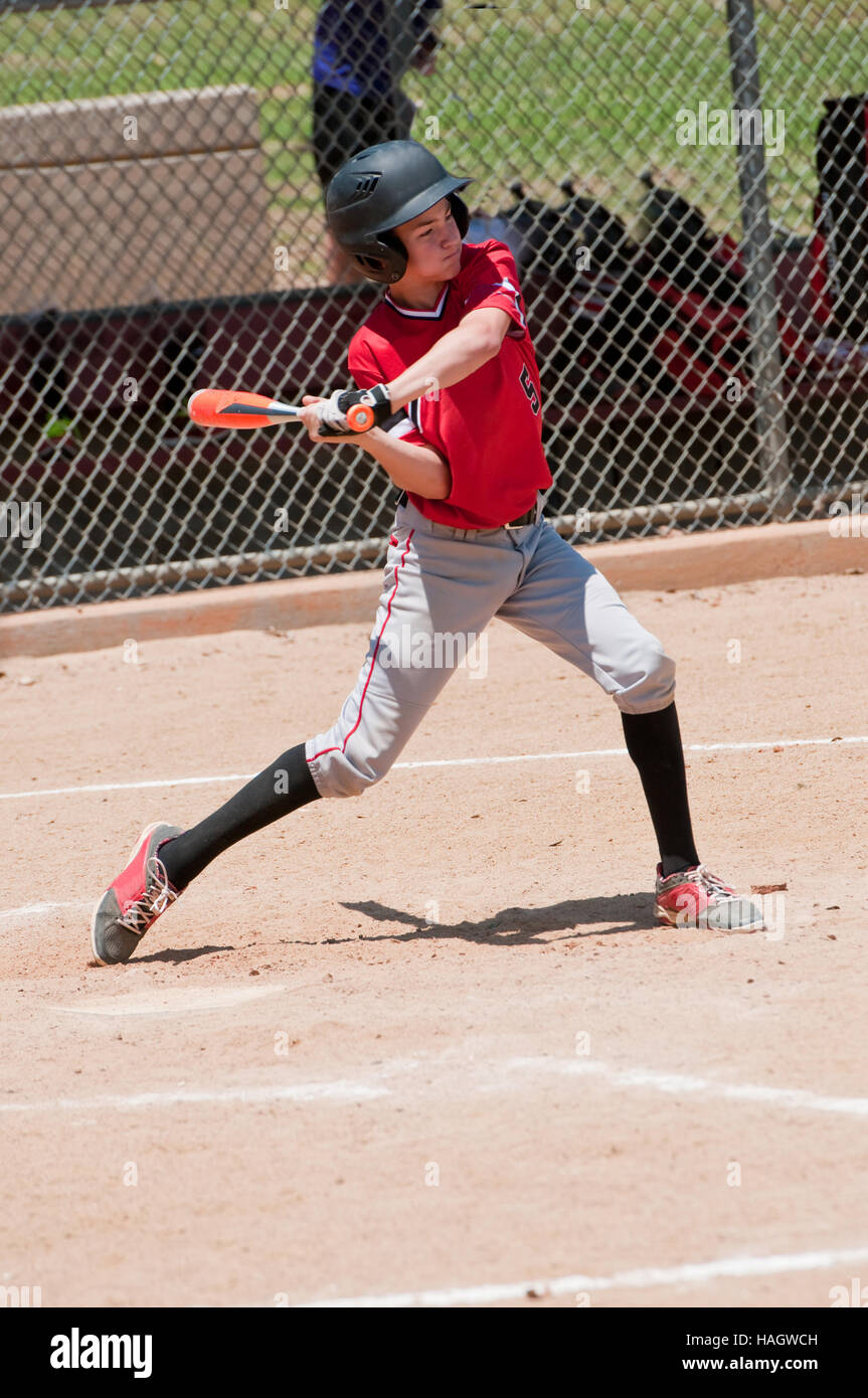 Youth baseball player swinging the bat to hit the ball. Stock Photo