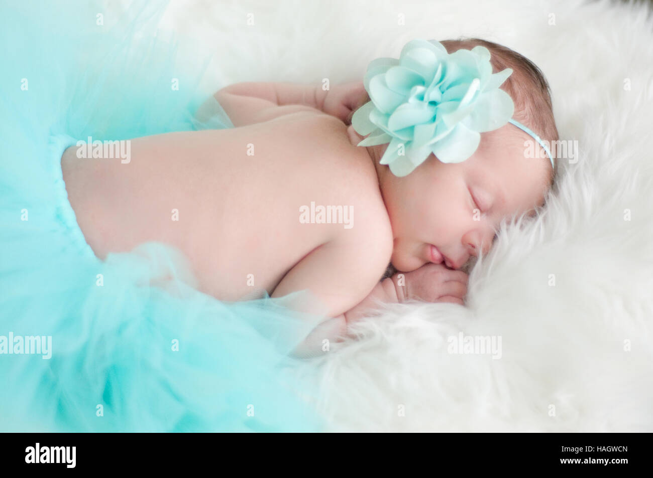 Precious baby girl sleeping in teal outfit laying on white fur. Stock Photo
