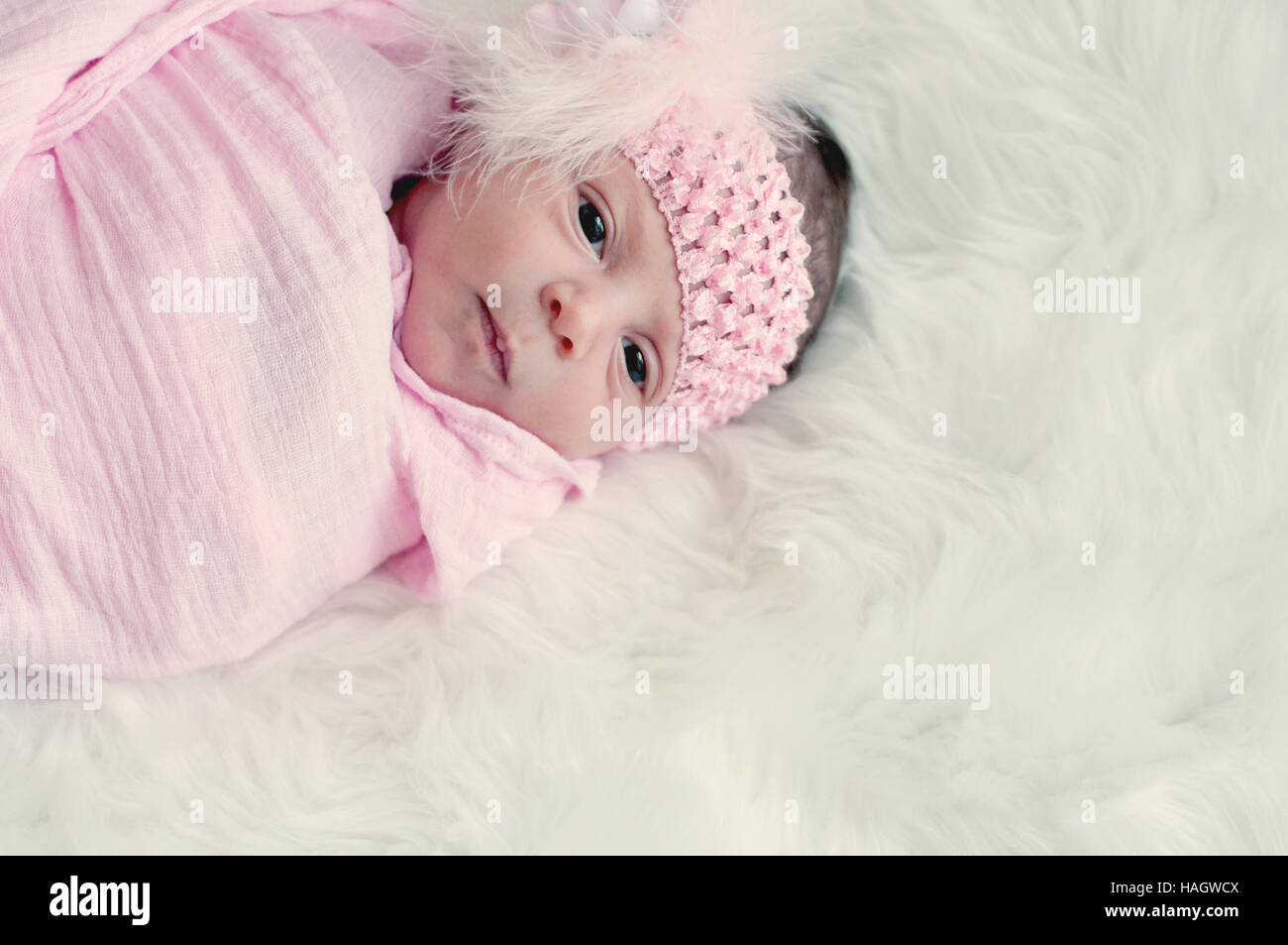 Newborn baby girl in pink headband laying on white fur with copy space. Stock Photo