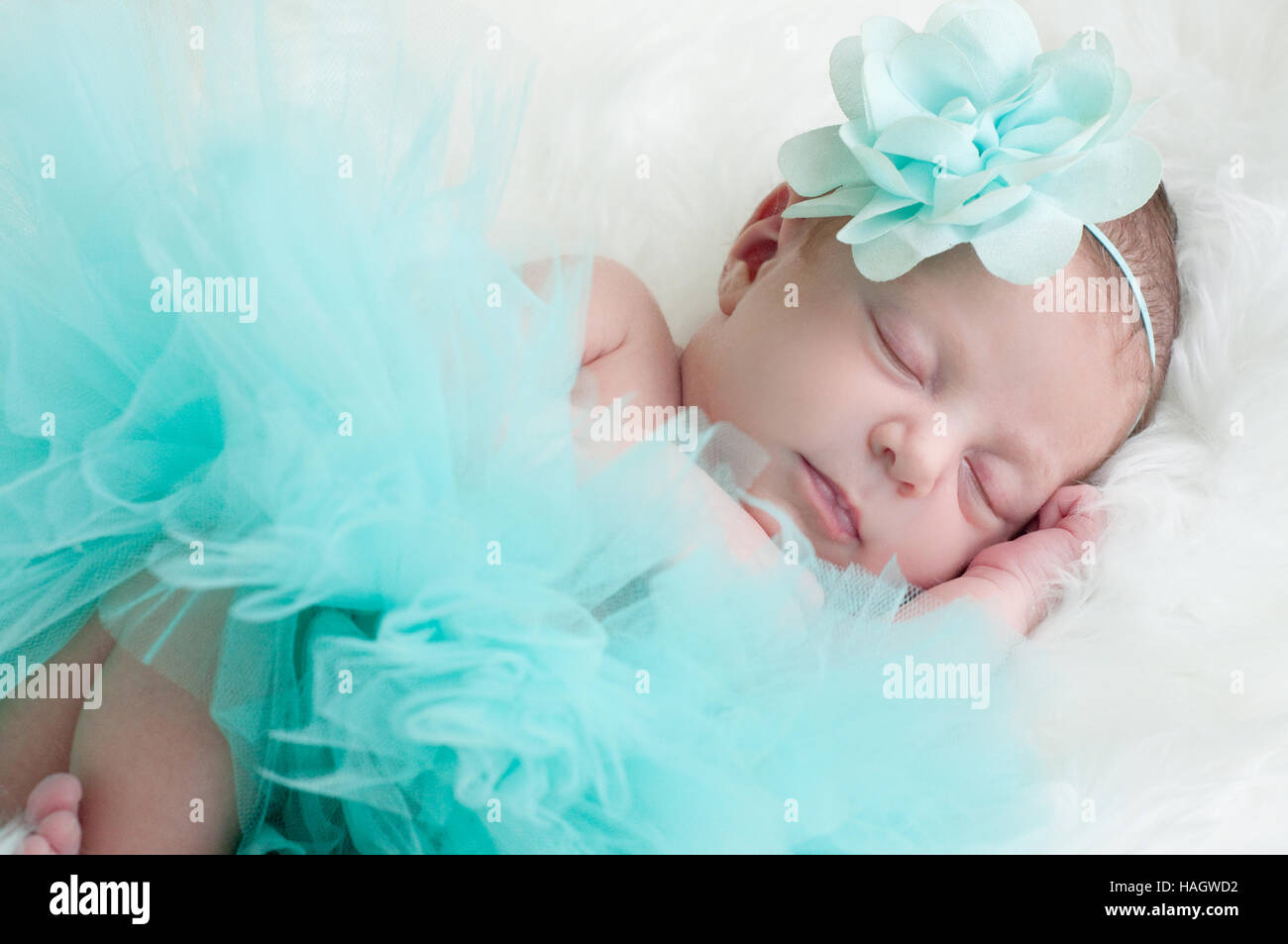 Precious baby girl sleeping in teal outfit laying on white fur. Stock Photo