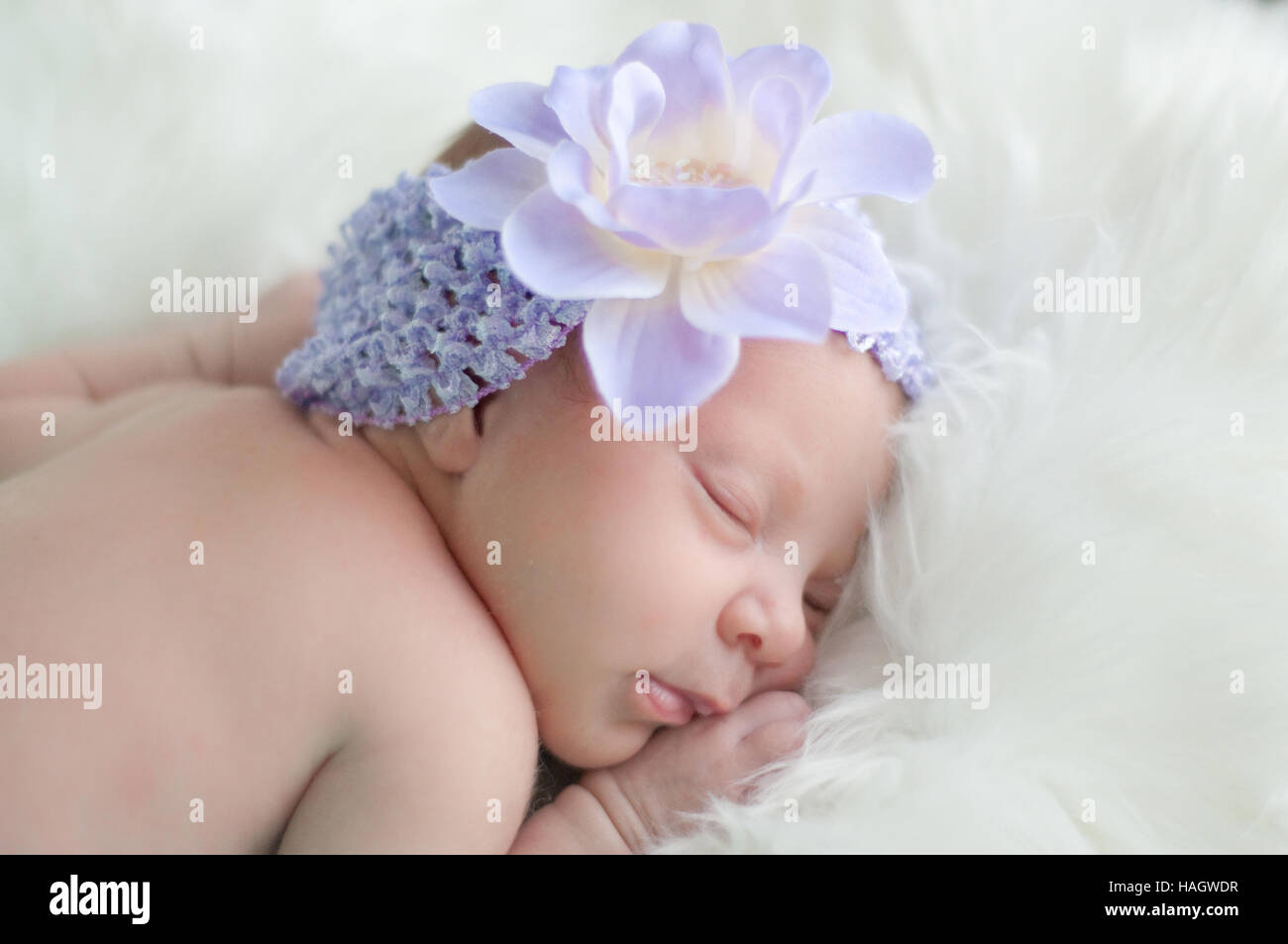 Precious baby girl sleeping in purple headband sleeping on white fur blanket. Stock Photo