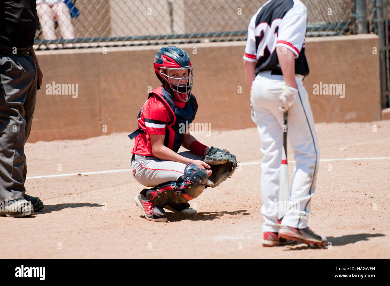 American youth baseball catcher looking at coach for signals with umpire behind him. Stock Photo
