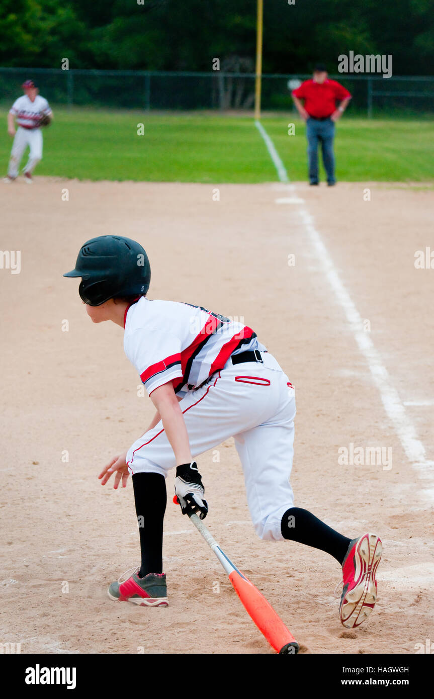 Teenage american baseball player sitting down bat to run to first base. Stock Photo