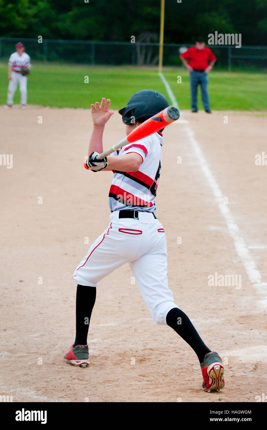 Teenage American baseball player swinging bat to hit the ball. Stock Photo