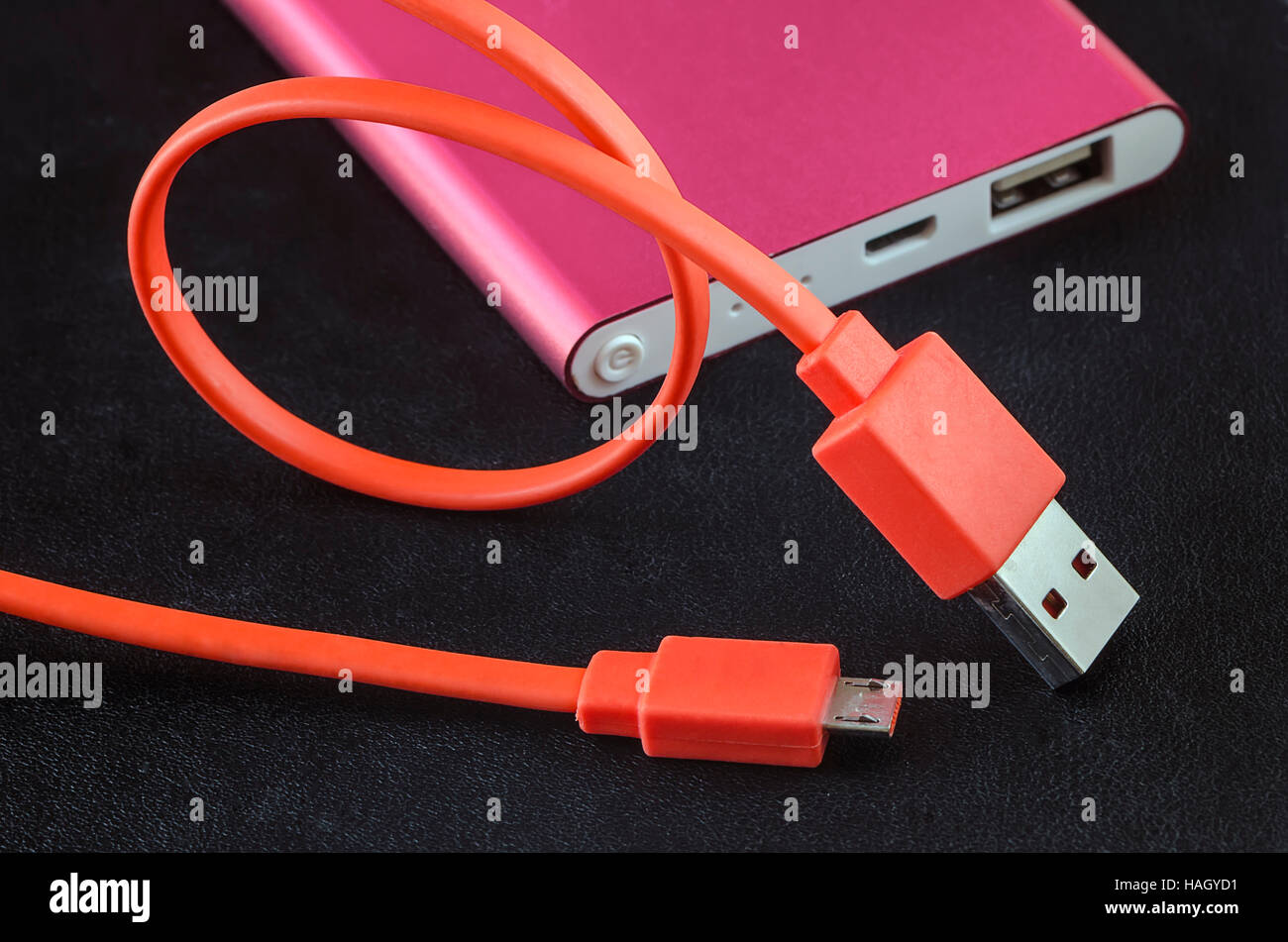 Orange color USB cable and red power bank on black leather background. Stock Photo